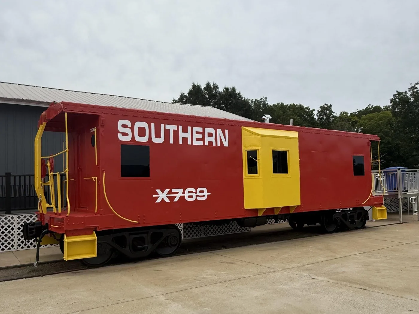 The freshly repainted red-and-yellow Southern X769 caboose beside the depot