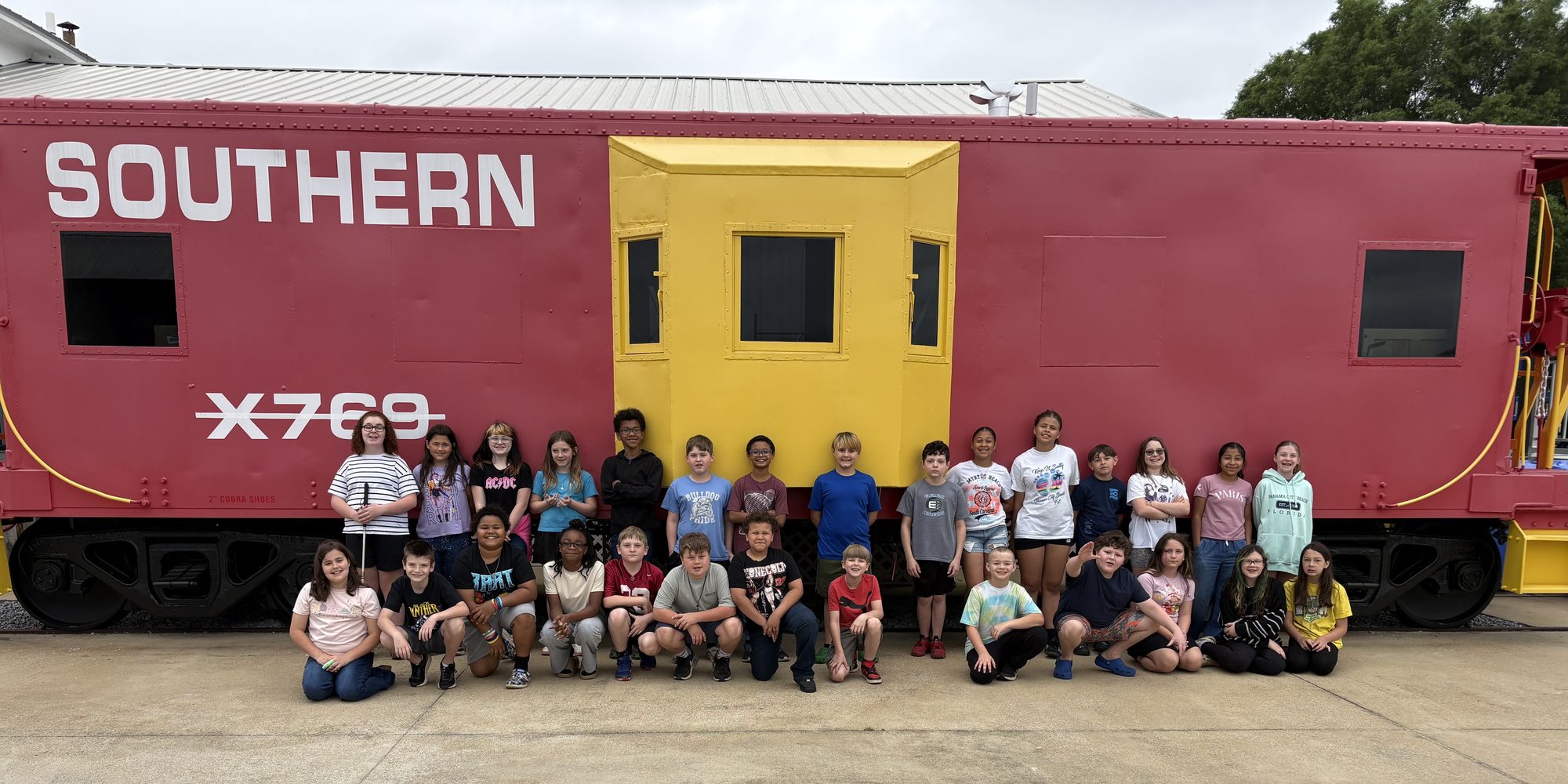 A visiting class poses in front of the museum's red-and-yellow Southern caboose