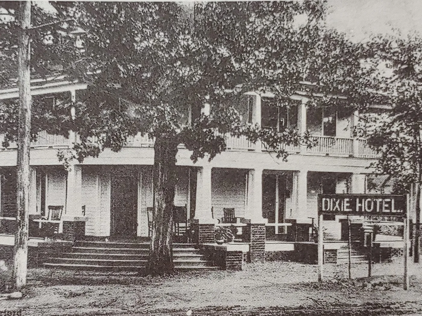 The two-story Dixie Hotel with its sign, shaded by a large tree