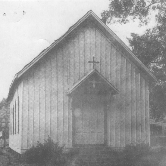 A small board-and-batten Episcopal church with a cross above the entry