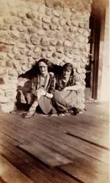 Two women seated on a porch floor against a stone fireplace
