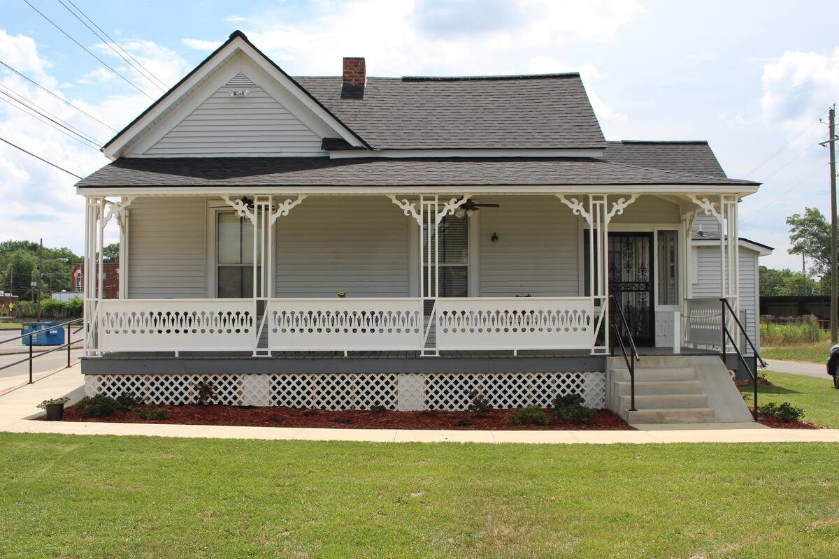 A restored white Victorian cottage with ornate gingerbread porch brackets