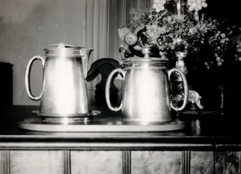 Two silver pitchers on a tray beside a floral arrangement